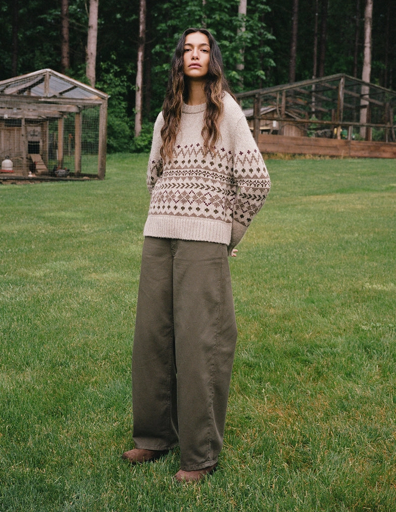 A woman in a patterned knit sweater and olive trousers standing on a green lawn