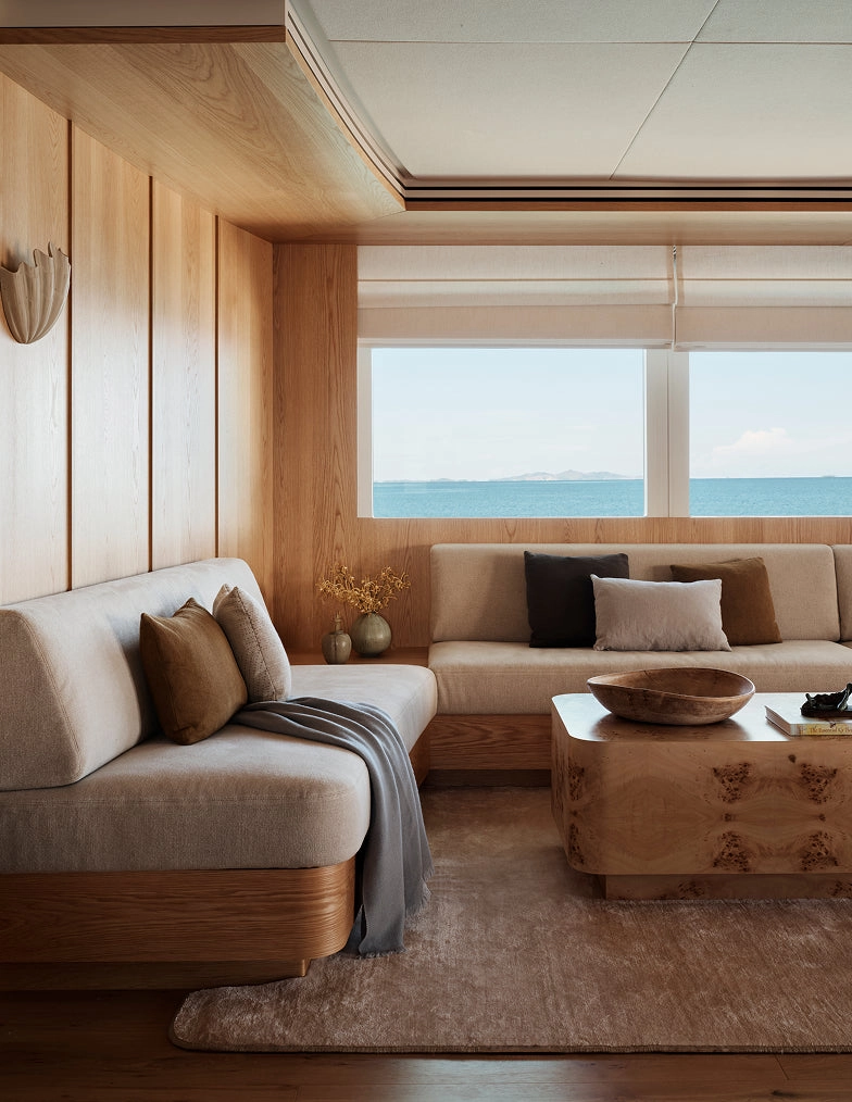 A living room with a low sectional, wood coffee table, and a view of the sea through the window