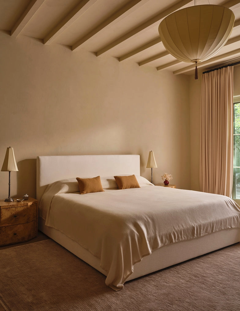A bedroom with a low bed, warm wood ceiling beams, and neutral linens