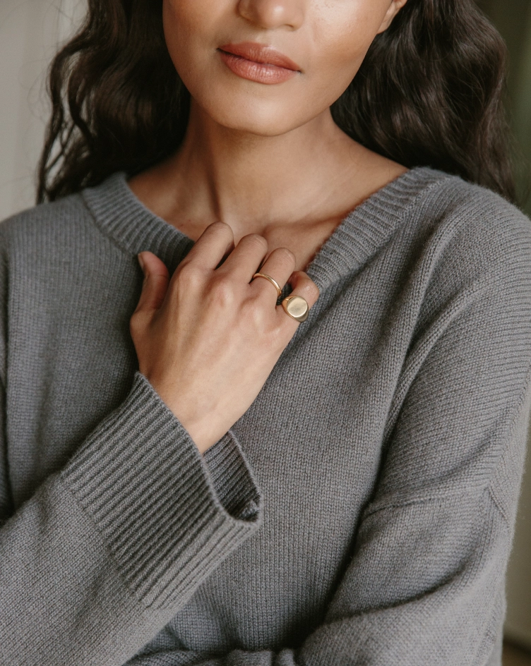Close view of a woman in a gray cashmere sweater with a hand resting at her collar and a gold ring