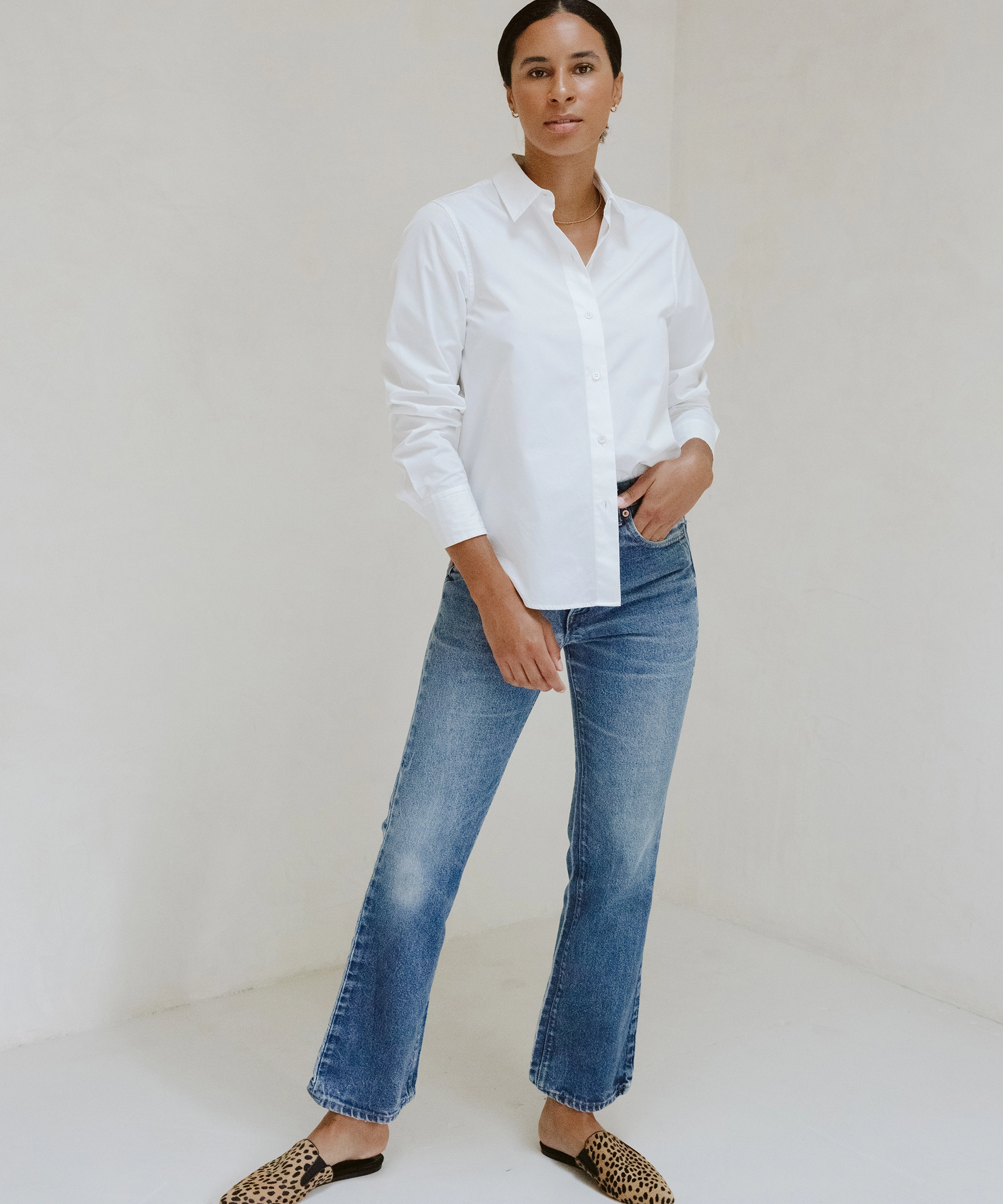 Model wearing a Jenni Kayne button-up with cheetah mules standing in front of a white wall