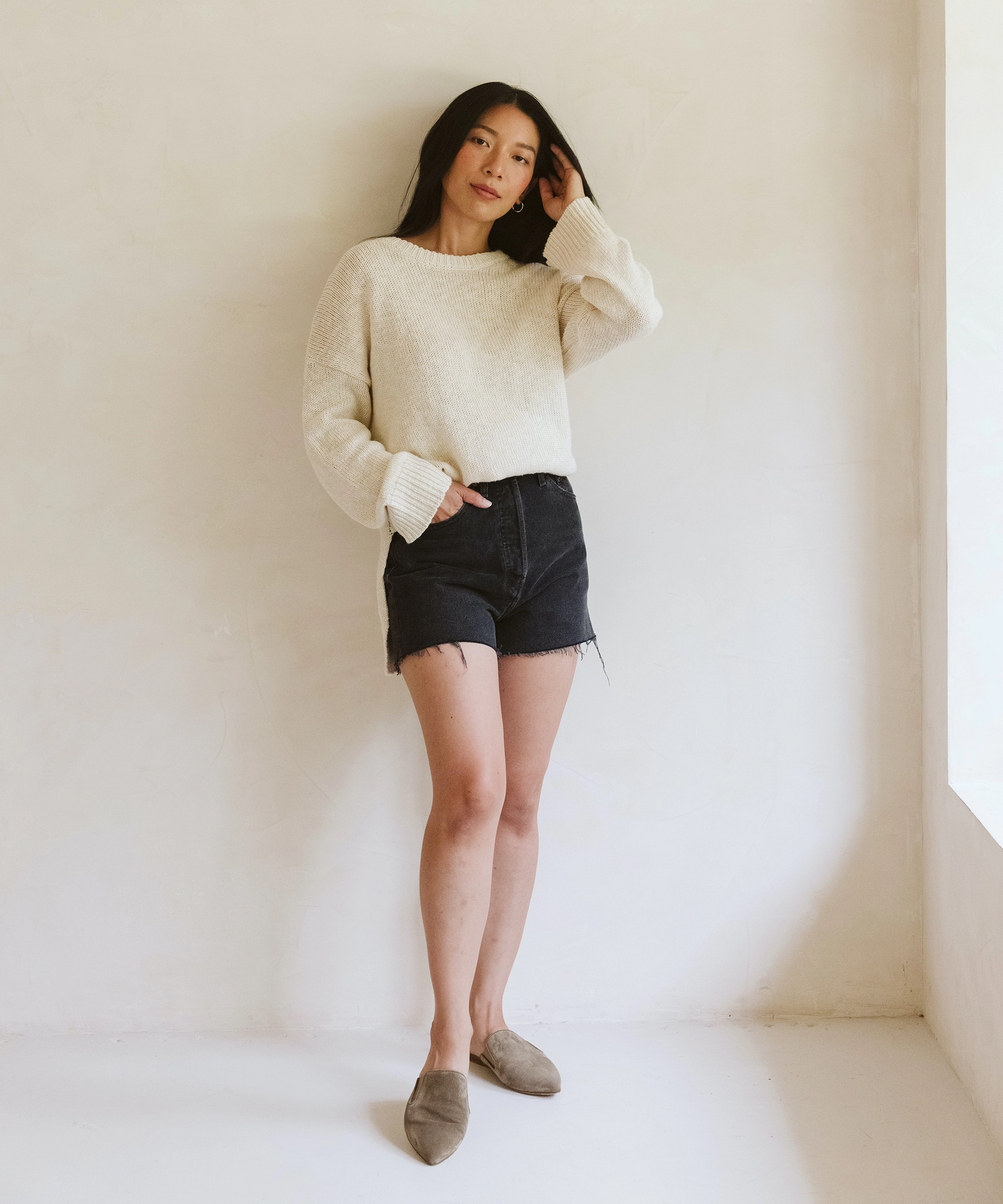 Model wearing a Jenni Kayne sweater and oiled leather mules in front of a white wall