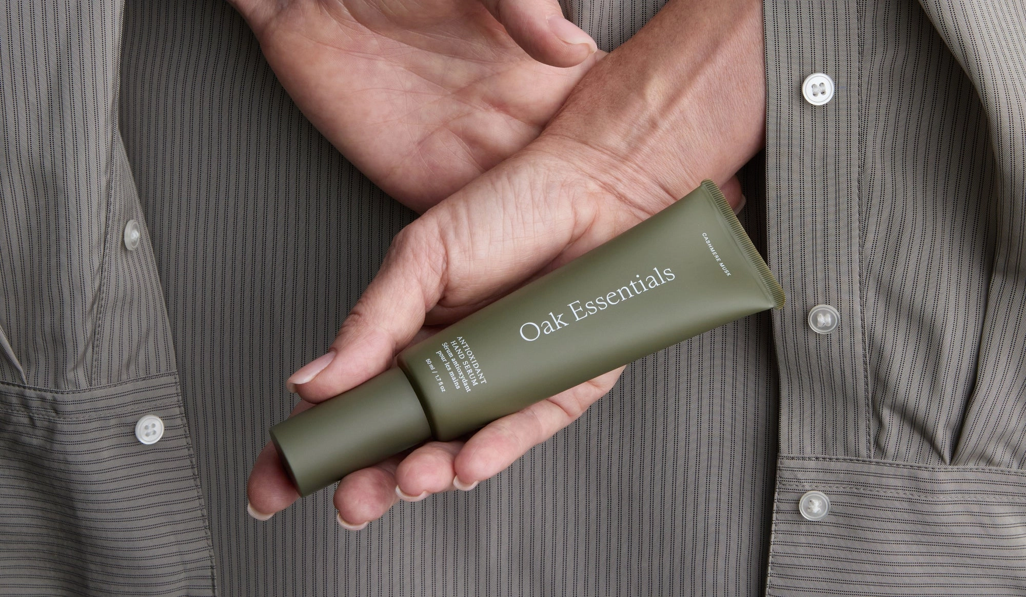 A hand holding a green tube of skincare against a gray striped shirt
